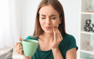 woman holding mug and touching jaw in discomfort